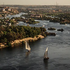 Feluccas sailing on the Nile at Aswan, with Elephantine Island and the city in the background.